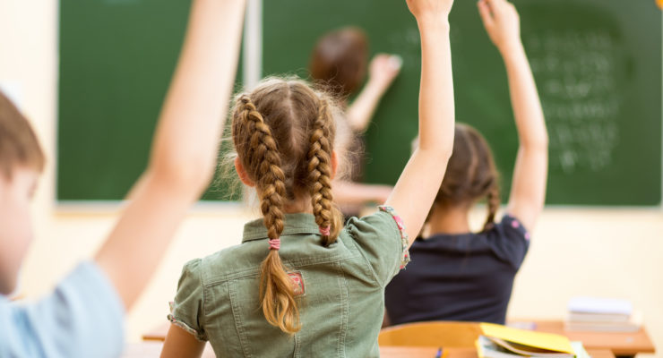 School children raising hands in classroom.