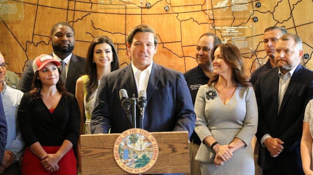 Governor Ron DeSantis standing at a podium speaking at the Audubon Corkscrew Swamp Sanctuary in Naples.