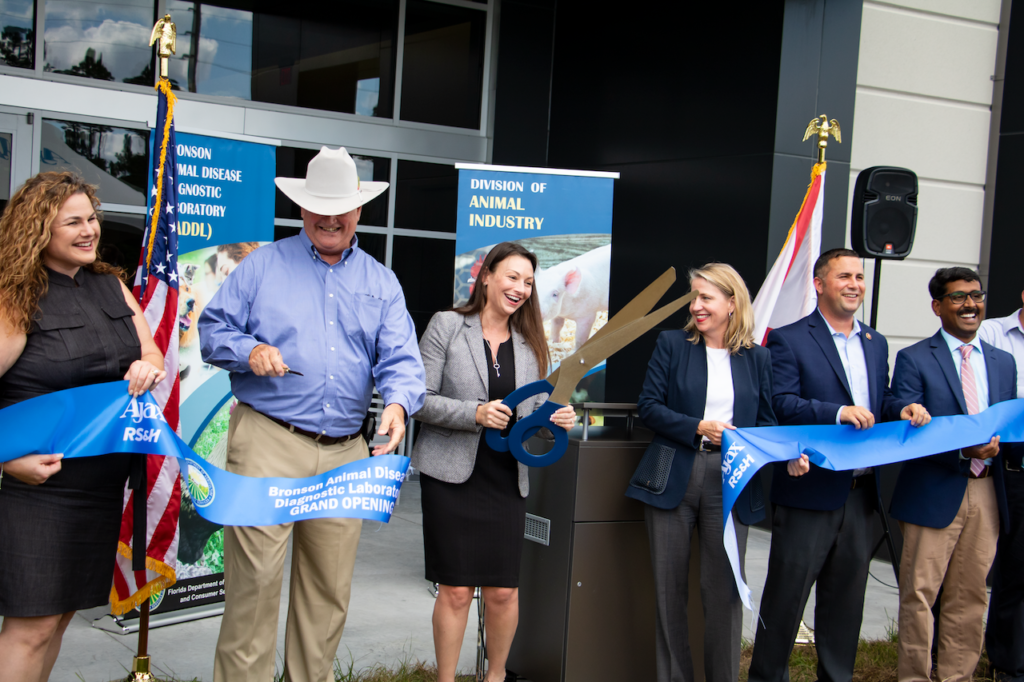 Commissioner Nikki Fried, holding an oversized pair of scissors, cuts the ribbon at today's grand opening of grand opening of the Bronson Animal Disease Diagnostics Laboratory.