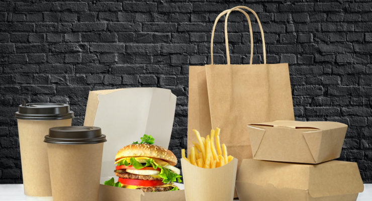 Fast food big lunch set of tasty hamburger, french fries, paper coffee cups, brown paper bag and box on the table near black brick wall background